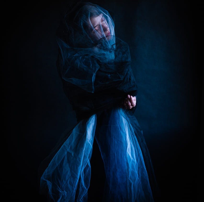woman in a dark room wearing a dark scarf and a lit skirt