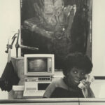 Black-and-white photo of a person answering phone with large painting in the wall behind them.
