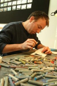 Eggleston seated at desk drawing with pastels.