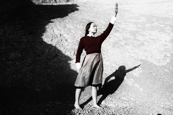 Woman on sandy beach waves at ships.