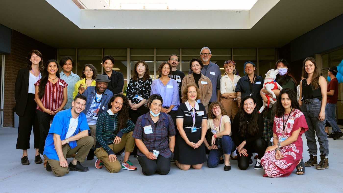 Group shot of new CalArts faculty members one row kneeling and one row of people standing in an outdoor courtyard