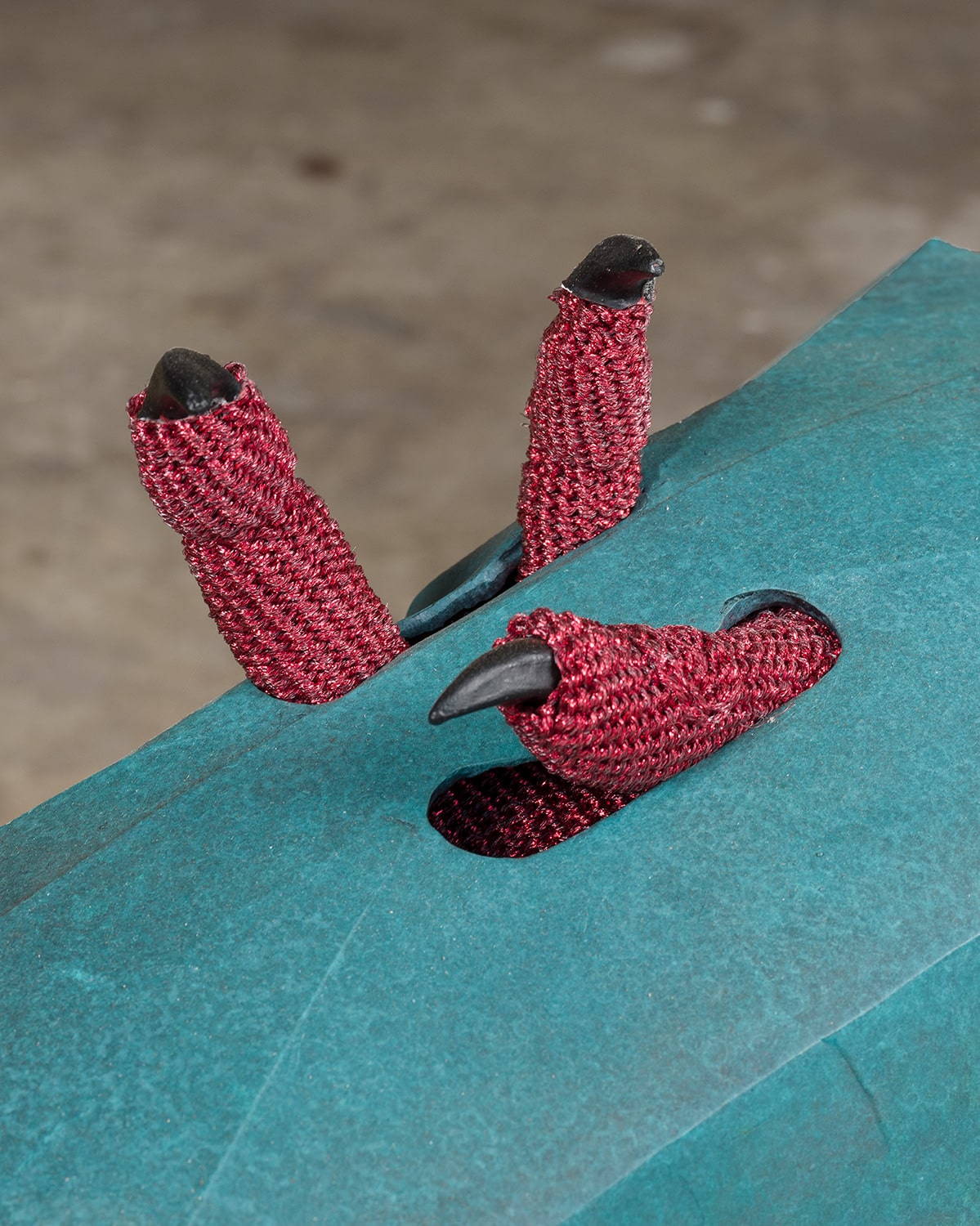 Red crocheted claws poke through a blue box.