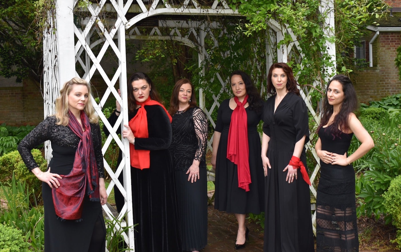 six women dressed mostly in black and red, standing outside under a lattice work