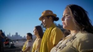 Trailer still of four individuals standing shoulder to shoulder.