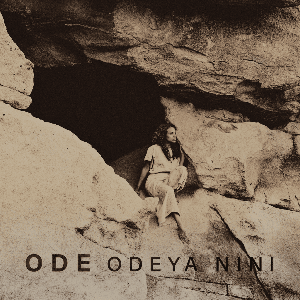 A woman sitting in front of a cave entrance in a sepia toned album cover