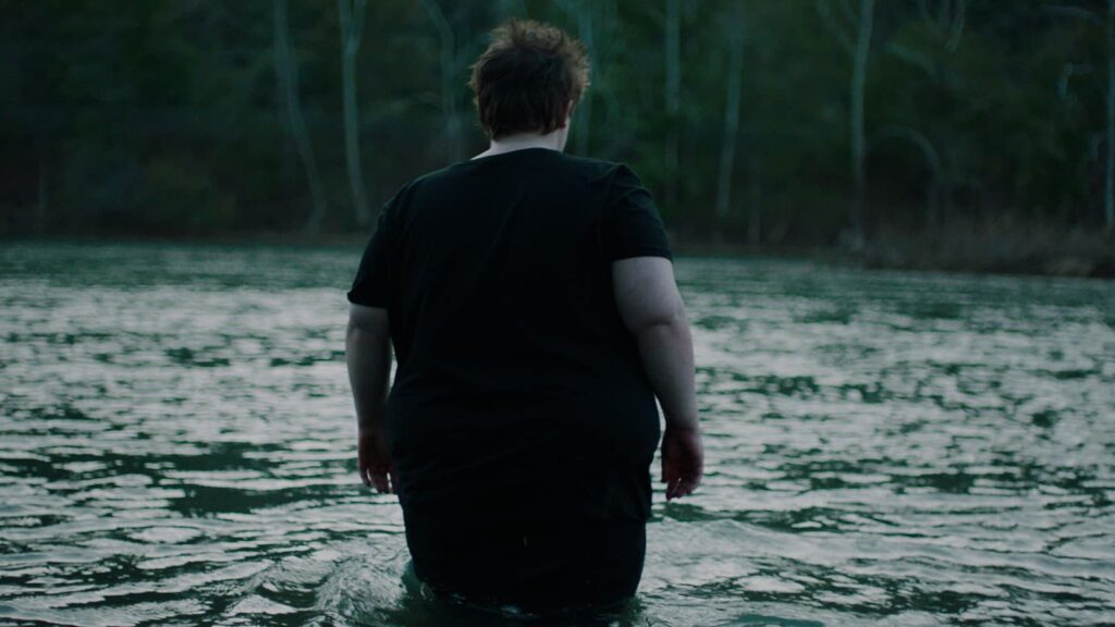 Person in black T-shirt standing knee-deep in a lake