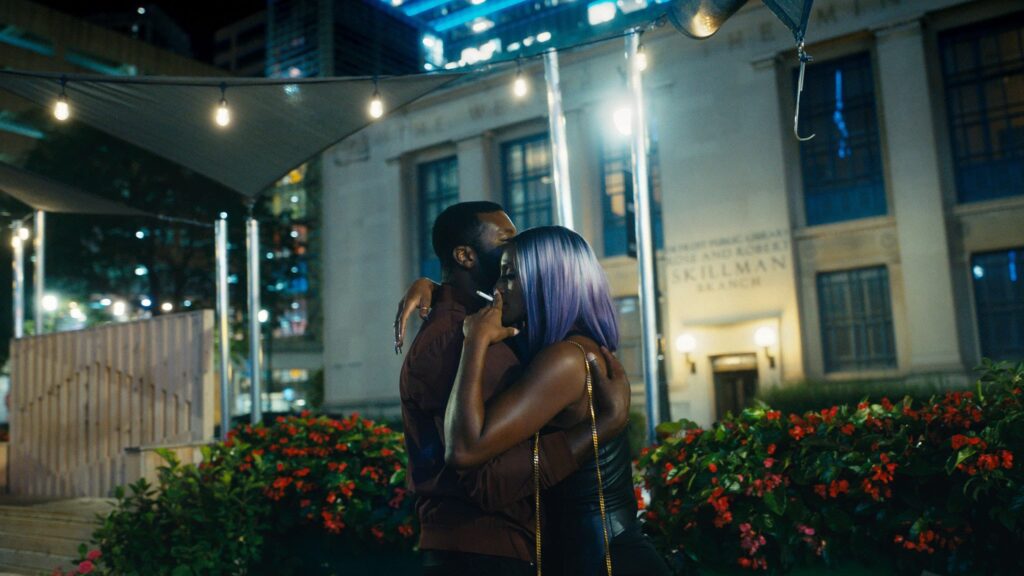 Two people embrace against a nighttime cityscape