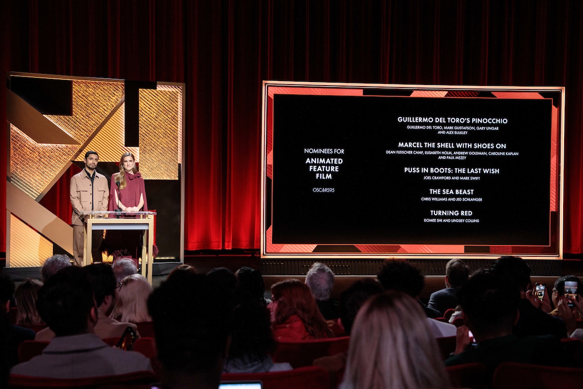 Two people stand at a podium at left while a screen at right details the nominees of Animated Feature Film Oscar.