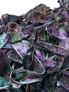 Mixed media assemblage of materials resembling purple and green flowers.