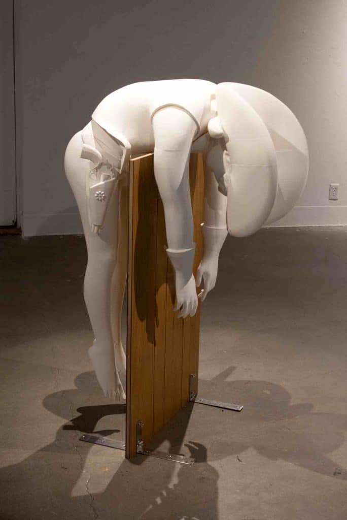 a white sculpture of a bent-over a wooden sign.