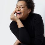 A portrait of a smiling Carrie Mae Weems, dressed in black.