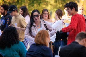 A group of people stand outside and chat. A woman at the centr