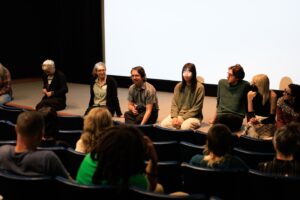 Eight people sit on the stage of the Bijou Theater, facing several peope in the audience.