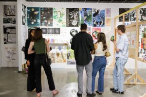 Five individuals look at gallery wall plastered with graphic design works and posters