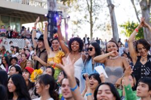 Row of students cheer with raised arms among crowd of graduation attendees