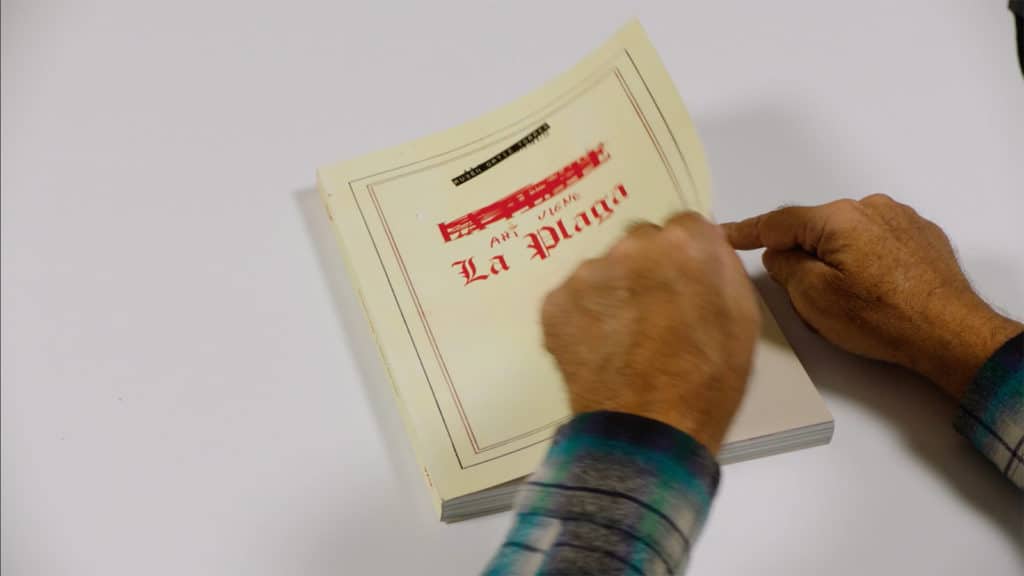 Person's hands turning over front cover of book titled 'Ahí viene la plaga'