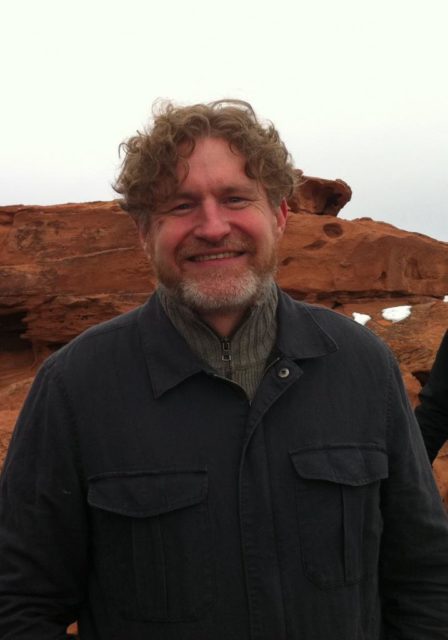 Brian Evenson smiles with red rock formation and overcast sky in background