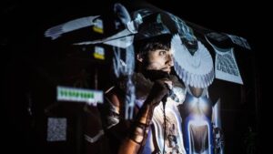 Peter Marks speaks into microphone amid a series of projected images on a dark stage.