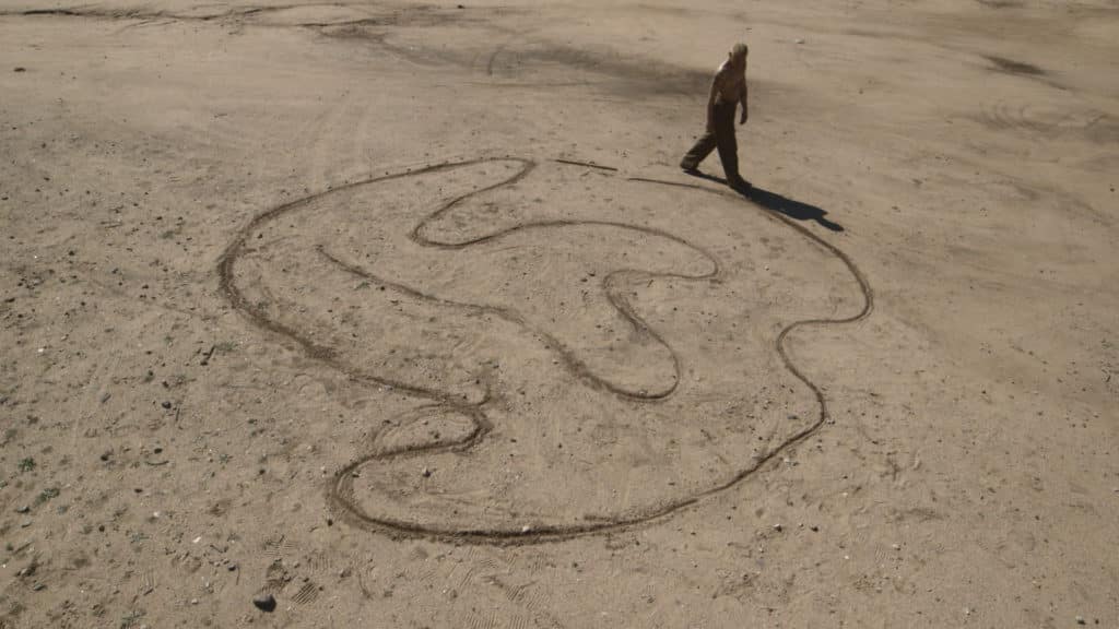Wide view of man walking by the edge of large serpentine pattern in the sand