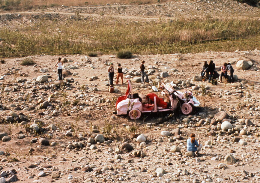 A pink-red dilapidated car from Suzanne Lacy's Car Renovation art project in 1972, set along the then desolate 126 freeway.
