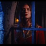Woman in red medieval attire looks out of darkened window