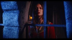 Woman in red medieval attire looks out of darkened window