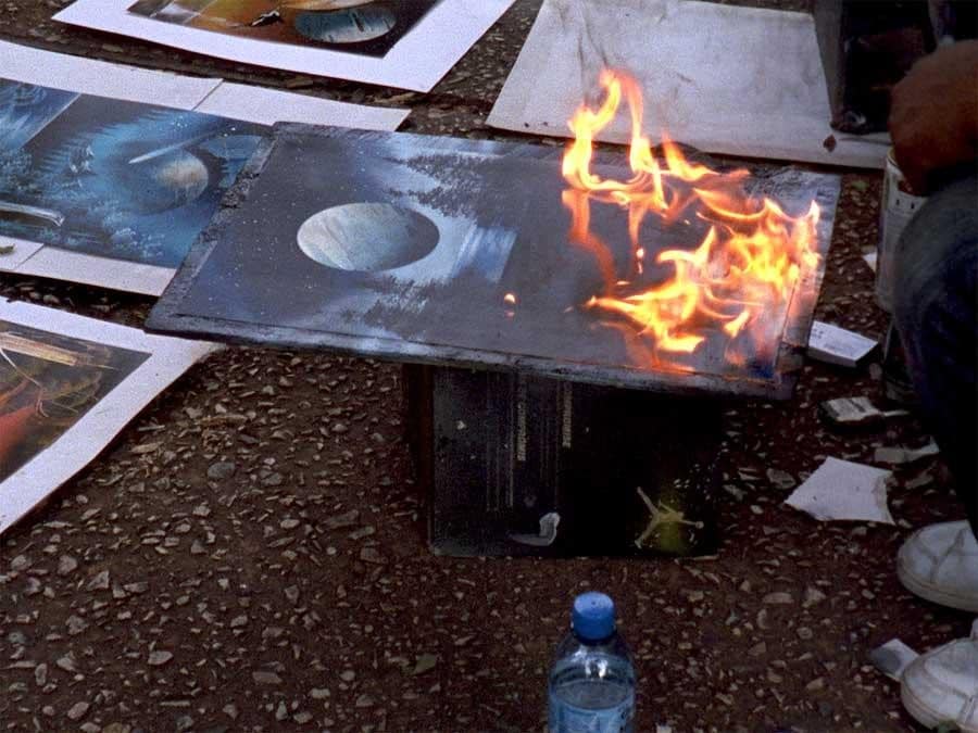 Various art prints on ground as a canvas with a moon and dark forest trees painting is set ablaze