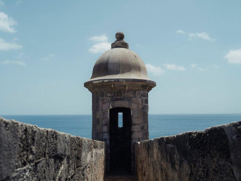 Stone walls flank entrance of domed cobble sentry box, with ocean and blue sky in the background
