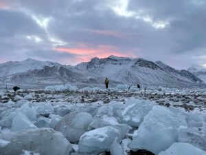 A film still of the desolate tundra of the Arctic Circle with one or two people seen in the distance.