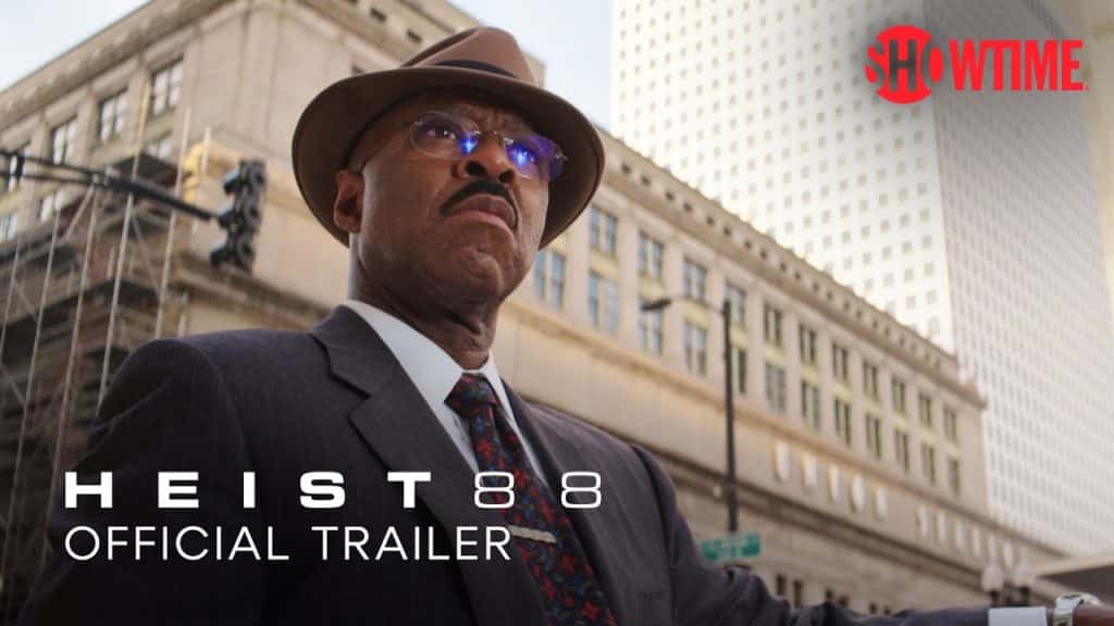 Courtney B. Vance as Jeremy Horne, wearing glasses, a hat, and suit and tie standing against multistory buildings