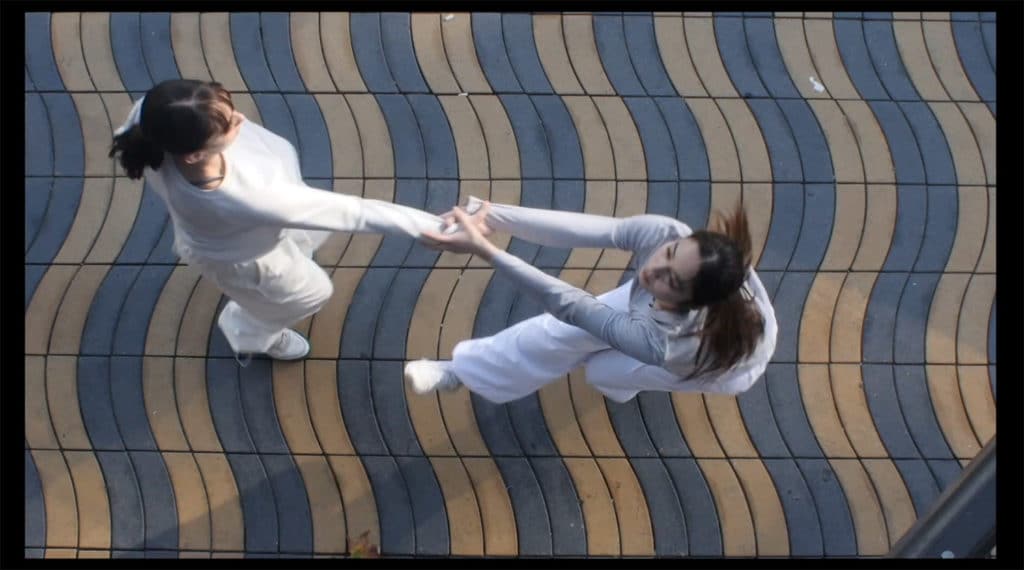 Aerial view of two female dancers wearing white performing on the sidewalk.
