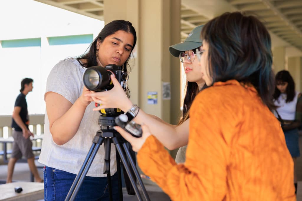 Three students in the Main Entrance setting up a camera on a tripod