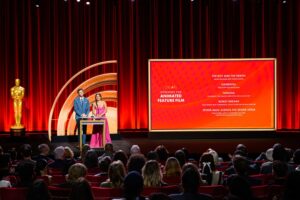Jack Quaid and Zazie Beetz at podium next to large screen depicting the nominees for Animated Feature Film