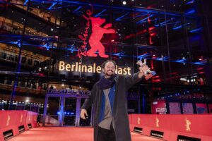 Director Nelson Carlos De Los Santos Arias holds up his Silver Bear at the Berlinale in front of the festival's venue.