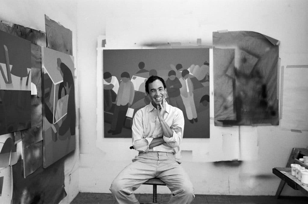 Geoff McFetridge sits smiling on a stool surrounded by his art