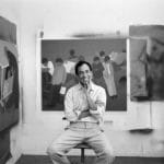Geoff McFetridge sits smiling on a stool surrounded by his art