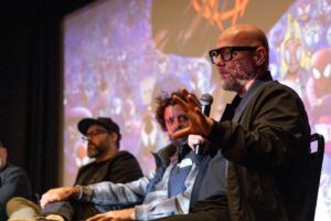 A man with with glasses speaks to an unseen audience from the stage.