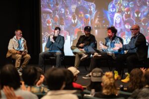 Five men sit on the Bijou Theater stage in front of a still image from Spider-Man: Across the Spider-Verse