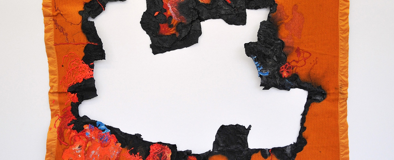 Orange tapestry against white wall with large geometric burn mark in the middle