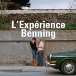 Still of two people talking on a sidewalk next to a parked green sedan with superimposed text 'L'Experience Benning'