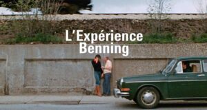 Still of two people talking on a sidewalk next to a parked green sedan with superimposed text 'L'Experience Benning'
