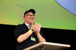 Pete Sohn, wearing black hat and glasses, claps at podium.