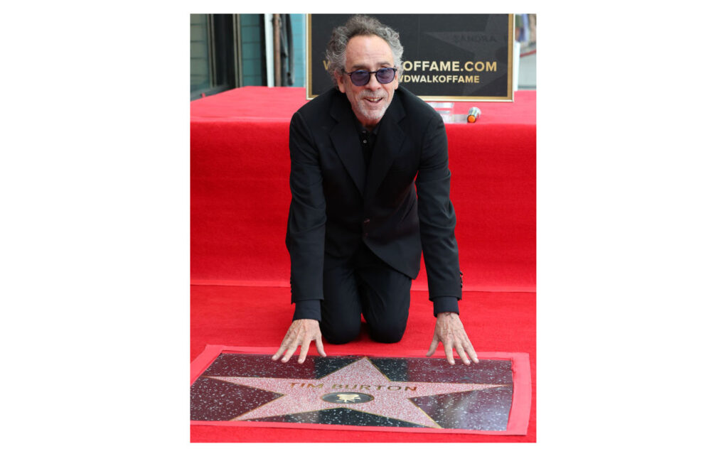 Tim Burton kneeling on a red carpet as he touches his star on the Hollywood Walk of Fame.