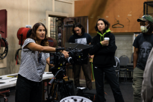 Professor instructs while holding camera as students listen