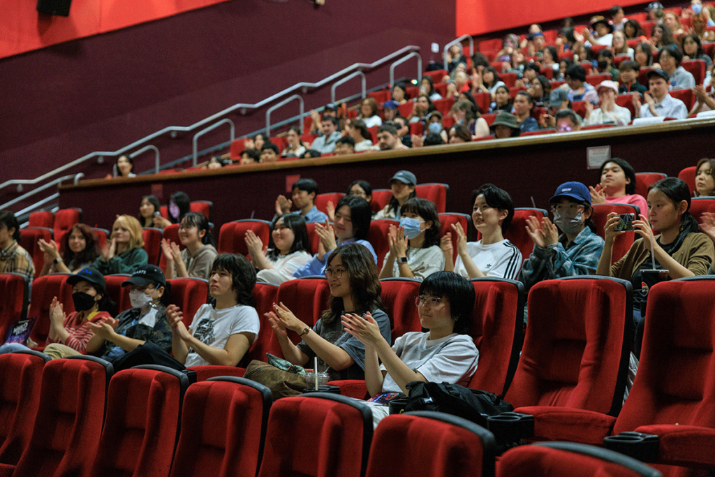 People applauding in red theater chairs.