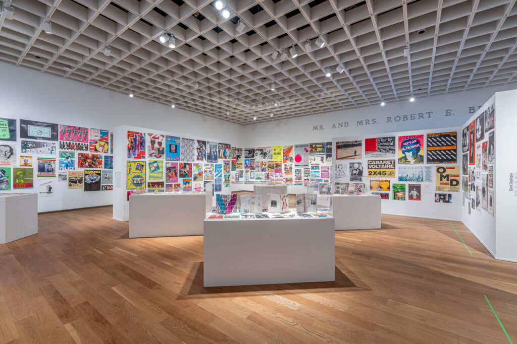 Gallery view of poster-adorned walls and various glass cases