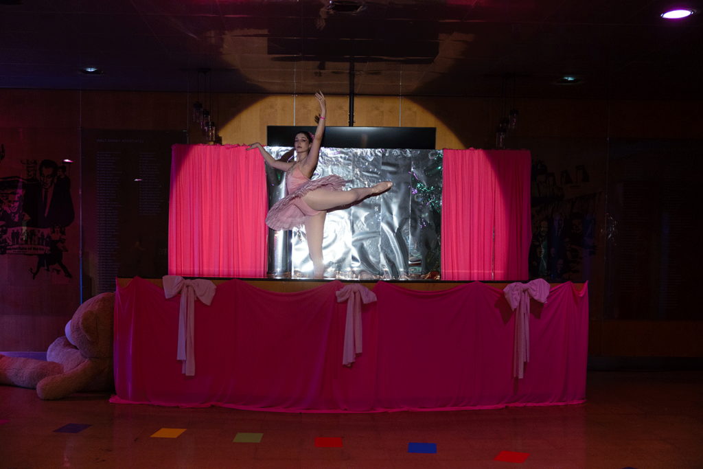 Spotlight shining on a ballerina doing an arabesque on a pink ribbon-adorned stage