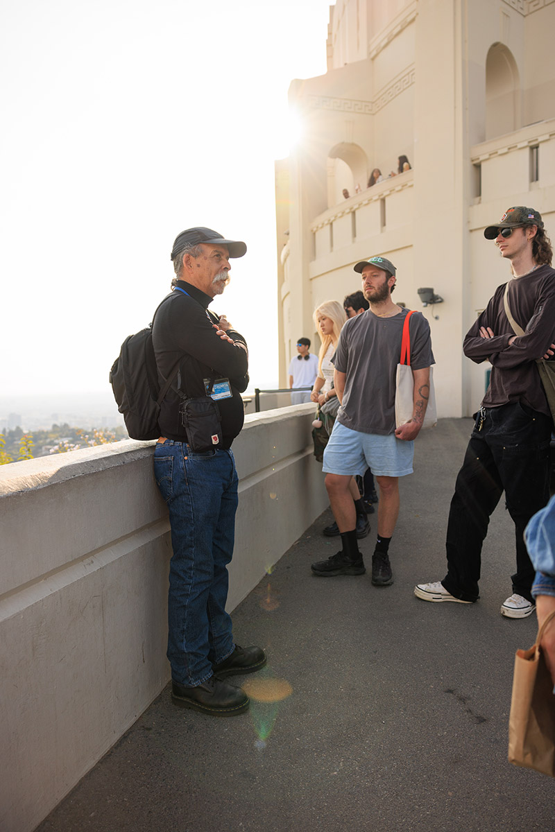 A teacher and a group of students stand near Griffith Observatory and observe the Los Angeles skyline