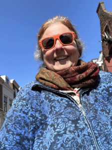 Cathy Tuttle, wearing red sunglasses, smiling with Dutch buildings in the background