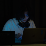 Junson Park in dark setting, lit by laptop screen and wearing headphones around neck